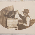 Lot 070 - Antique Unmounted Paper Photograph Of Old Man Petting Cat Standing On Crates, Postcard Style Paper
