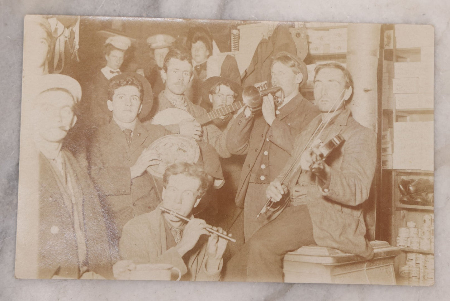 Lot 105 - Antique Real Photo Postcard R.P.P.C. Of Band Including Flute, Fiddle And Banjo, Playing While Crowded Into A Corner Of Storage Room, With Other Men And Women In Background, Circa 1910