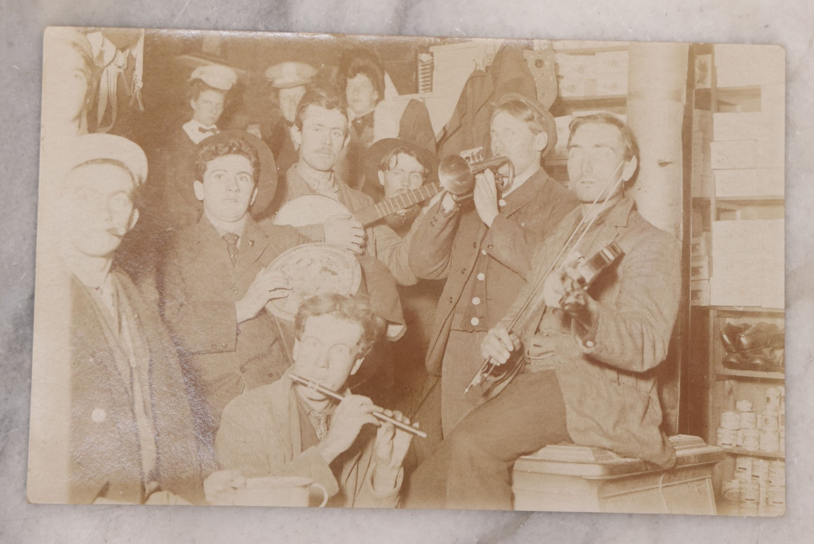 Lot 105 - Antique Real Photo Postcard R.P.P.C. Of Band Including Flute, Fiddle And Banjo, Playing While Crowded Into A Corner Of Storage Room, With Other Men And Women In Background, Circa 1910