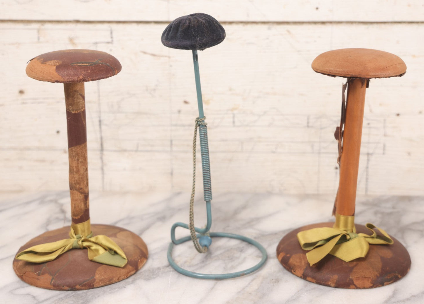 Lot 029 - Trio Of Vintage Hat Stands Including Two With Partial Fabric Coverings And Greenish-Yellow Ribbons, And One Blue Wire Stand With Felt Pillow