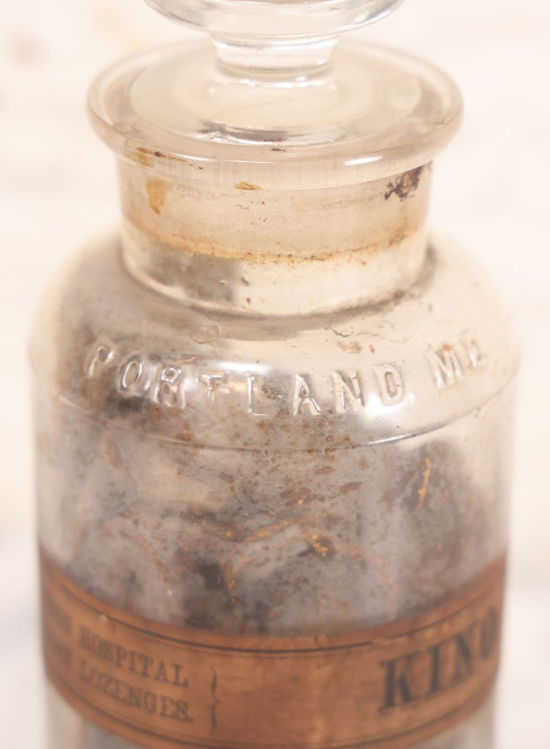 Lot 058 - Antique Apothecary Bottle With Original Paper Label “Kino, London Hospital Throat Lozenges” With Contents, Clear Glass Bottle With Stopper Manufactured By George C. Frye, Portland, Maine, 8" H