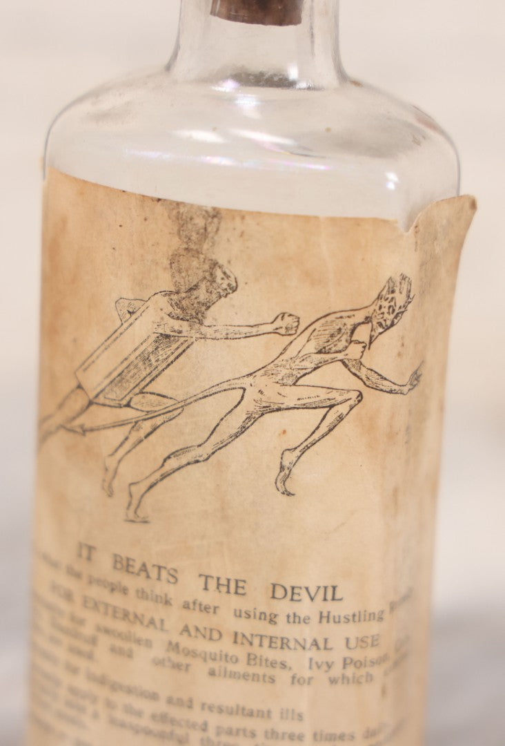 Lot 060 - Antique Clear Glass Bottle With Paper Label “It Beats The Devil” Showing Devil Race Graphics, Arthur N. Roe, Branchville, New Jersey, 5-1/2" H