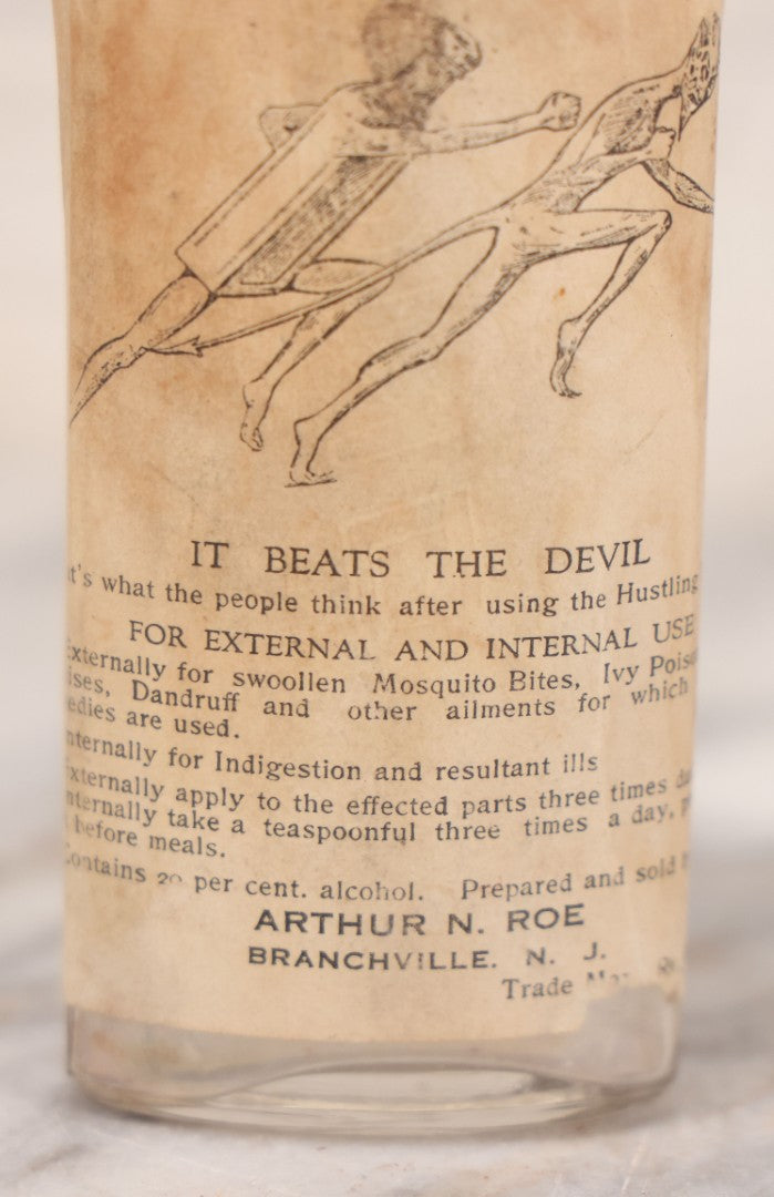 Lot 060 - Antique Clear Glass Bottle With Paper Label “It Beats The Devil” Showing Devil Race Graphics, Arthur N. Roe, Branchville, New Jersey, 5-1/2" H