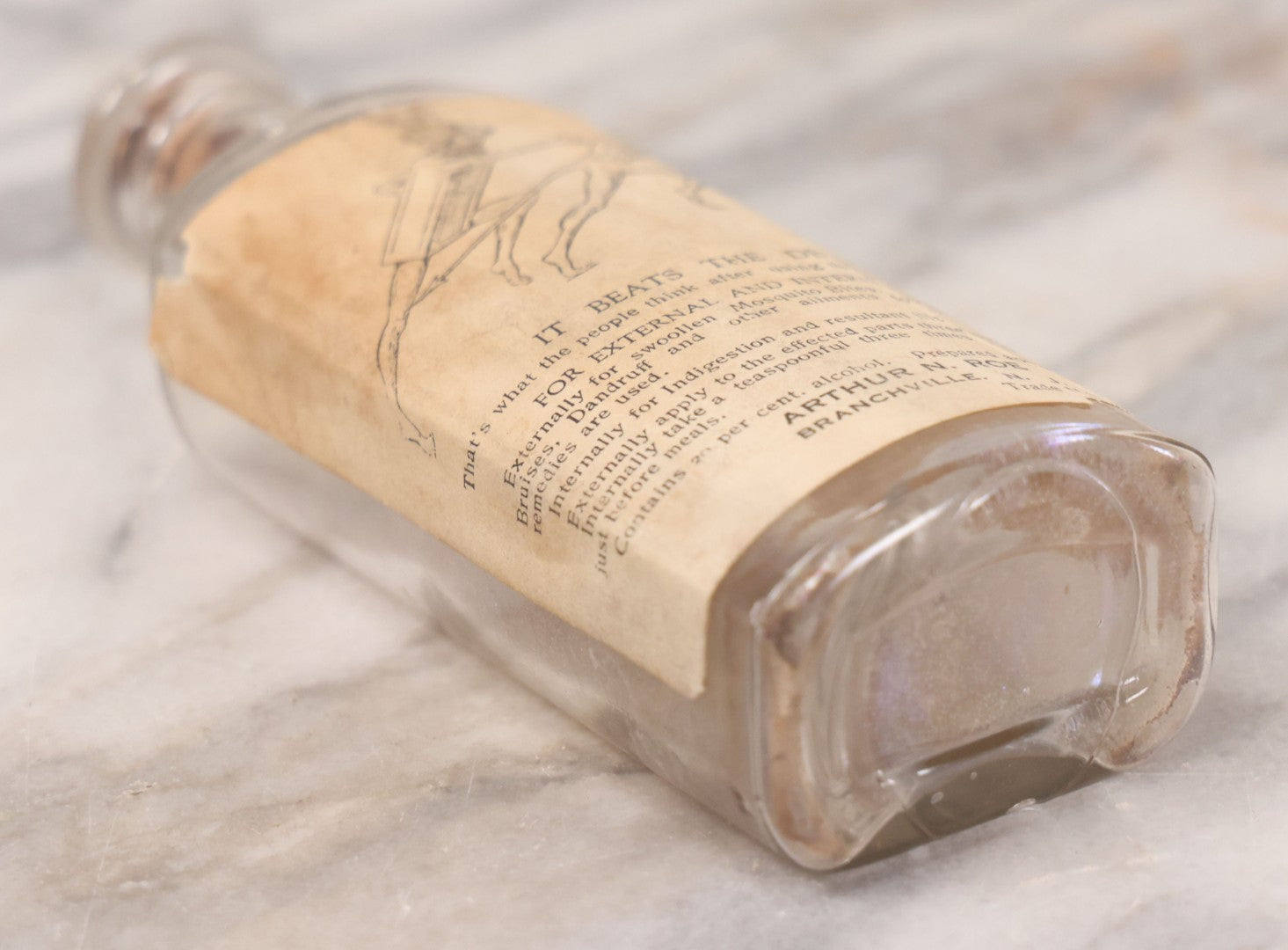 Lot 060 - Antique Clear Glass Bottle With Paper Label “It Beats The Devil” Showing Devil Race Graphics, Arthur N. Roe, Branchville, New Jersey, 5-1/2" H