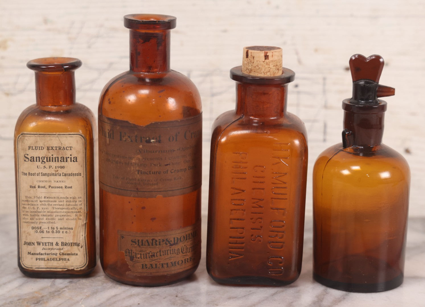 Lot 075 - Grouping Of Four Antique Amber Glass Bottles Including Cramp Bark From Sharp & Dohme, Baltimore, Sanguinaria From John Wyeth & Brother, Philadelphia, H.K. Mulford Co., Philadelphia, And One Unmarked With Stopper