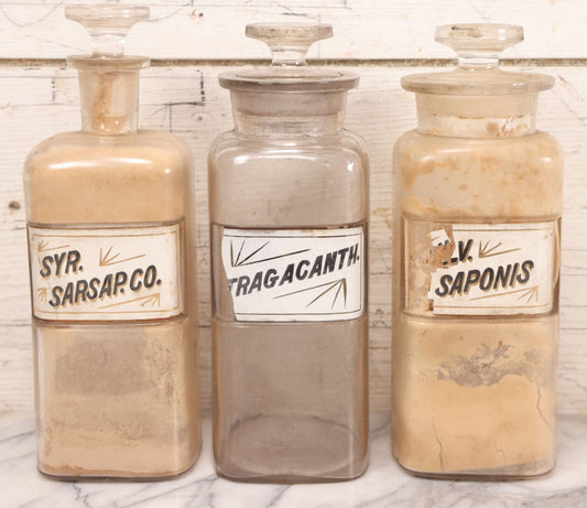 Lot 080 - Grouping Of Three Antique Whitall Tatum Co. Clear Glass Apothecary Bottles With Stoppers And Partial Reverse Painted Labels Including Syr. Sarsap. Co., Saponis, And Tragacanth