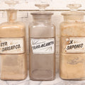 Lot 080 - Grouping Of Three Antique Whitall Tatum Co. Clear Glass Apothecary Bottles With Stoppers And Partial Reverse Painted Labels Including Syr. Sarsap. Co., Saponis, And Tragacanth