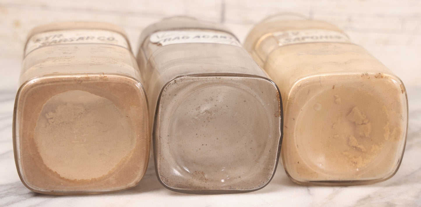 Lot 080 - Grouping Of Three Antique Whitall Tatum Co. Clear Glass Apothecary Bottles With Stoppers And Partial Reverse Painted Labels Including Syr. Sarsap. Co., Saponis, And Tragacanth