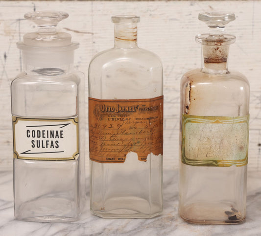 Lot 081 - Grouping Of Three Antique Clear Glass Apothecary Bottles Including Codeinae Sulfas F&S St. Louis, Bottle With Illegible Paper Label, And Otto Jafnel Pharmacist Liberty Ny
