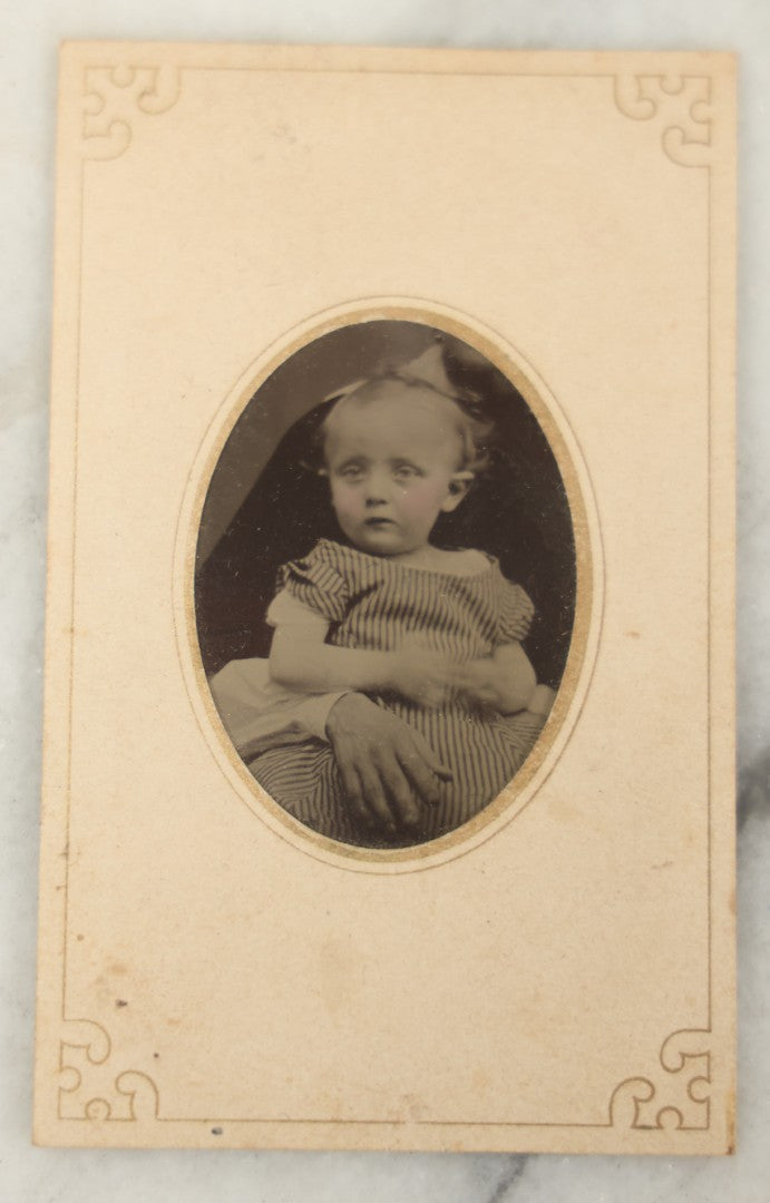 Lot 019 - Antique Not-So-Hidden Mother Tintype Photograph Of A Blonde Toddler In Striped Dress With Mother's Hand, Chin Visible, In Paper Frame