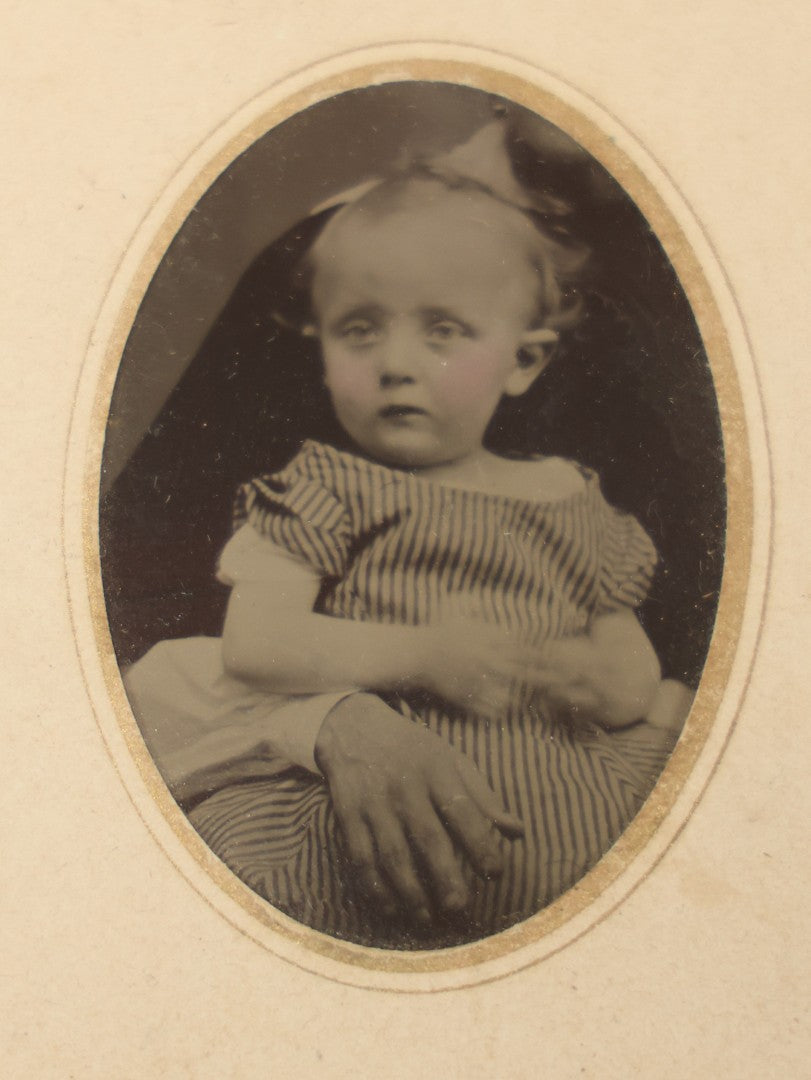 Lot 019 - Antique Not-So-Hidden Mother Tintype Photograph Of A Blonde Toddler In Striped Dress With Mother's Hand, Chin Visible, In Paper Frame