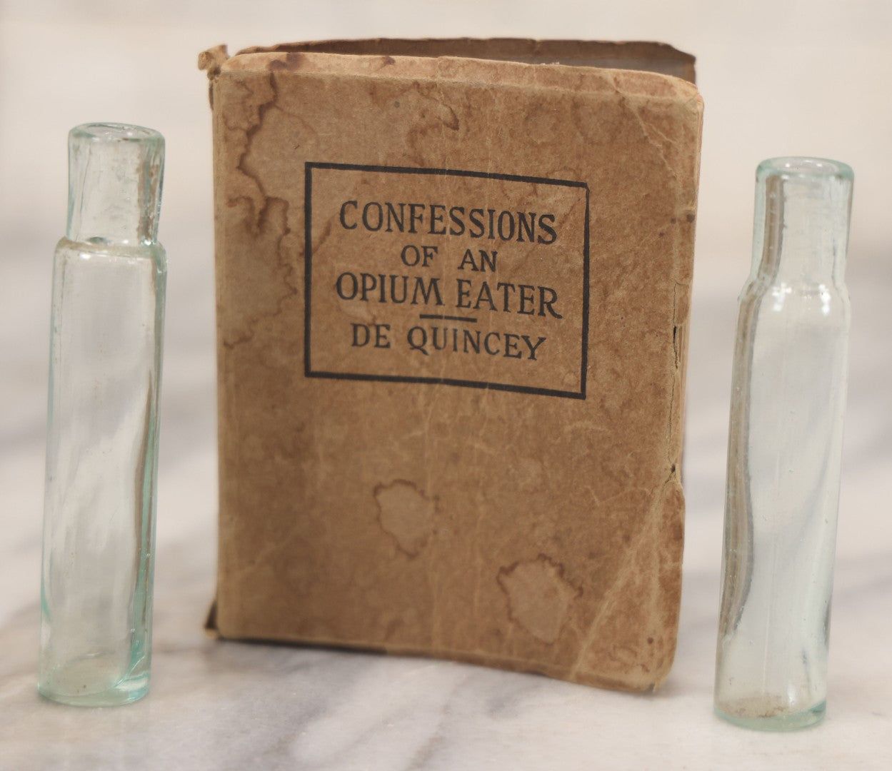 Lot 041 - Grouping Of Two Miniature Narrow Clear Glass Bottles And "Confessions Of An Opium Eater" Antique Miniature Book With Paper Cover And Advertising For Whitman's Candy In Rear, Published By Little Leather Library Corporation, New York, Circa 1920
