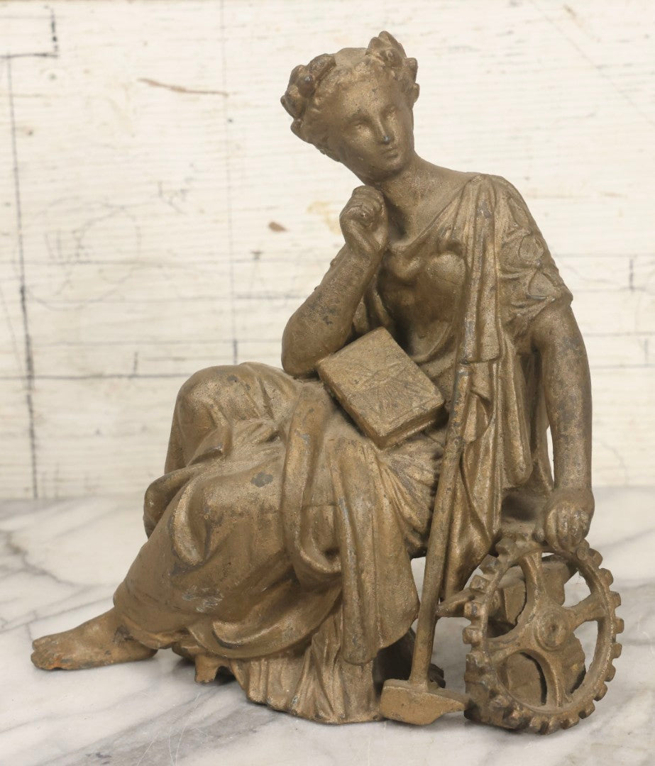 Lot 057 - Antique Cast Spelter Metal Clock Topper Statue With Bronze Wash Depicting Goddess-Like Woman Beside Gear, Anvil, And Blacksmith's Hammer, 8-1/2" H