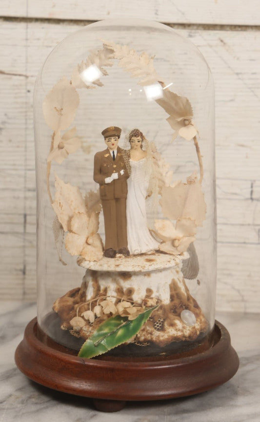 Lot 035 - Vintage Wwii Era Servicemember Wedding Cake Topper In Glass Dome Cloche With Bride, Groom In Military Uniform, Faux White Flowers, And Wood Base, 9-1/2" H