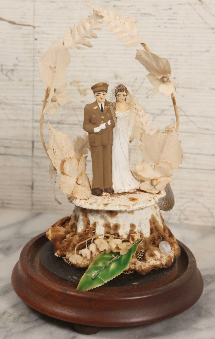 Lot 035 - Vintage Wwii Era Servicemember Wedding Cake Topper In Glass Dome Cloche With Bride, Groom In Military Uniform, Faux White Flowers, And Wood Base, 9-1/2" H