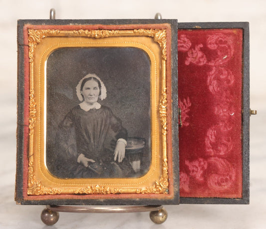 Lot 047 - Antique 1/6th Plate Ruby Ambrotype Photograph Of Elderly Woman In White Bonnet Holding Object, Possibly A Book, In Full Split Leatherette Union Case
