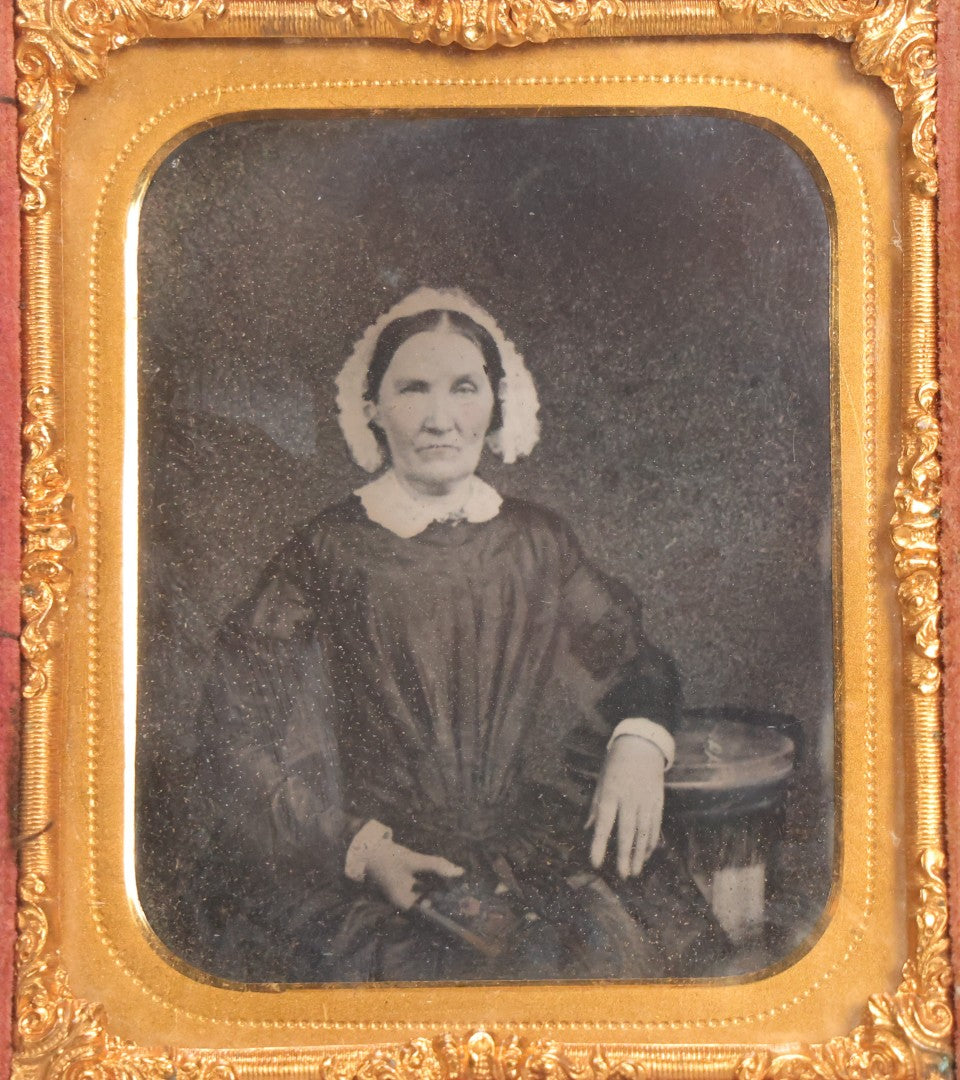 Lot 047 - Antique 1/6th Plate Ruby Ambrotype Photograph Of Elderly Woman In White Bonnet Holding Object, Possibly A Book, In Full Split Leatherette Union Case