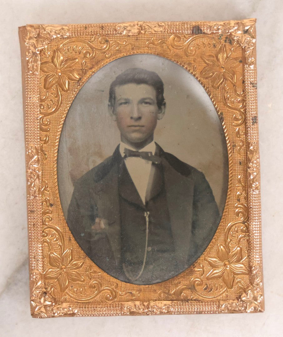 Lot 061 - Antique 1/9th Plate Hand-Tinted Tintype Photograph Of Thin Young Man With Bowtie And Vest Chain, Uncased With Brass Mat And Preserver