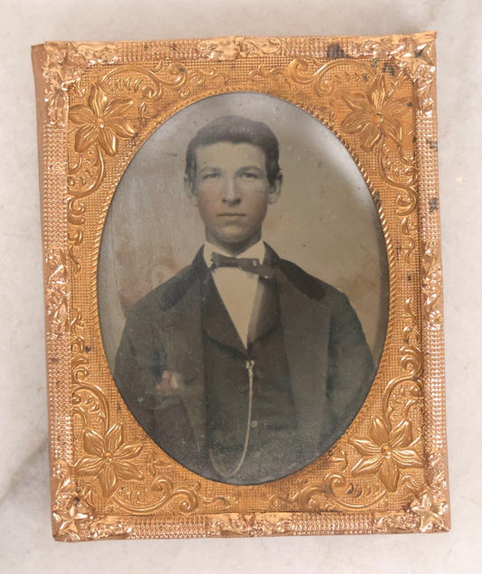 Lot 061 - Antique 1/9th Plate Hand-Tinted Tintype Photograph Of Thin Young Man With Bowtie And Vest Chain, Uncased With Brass Mat And Preserver