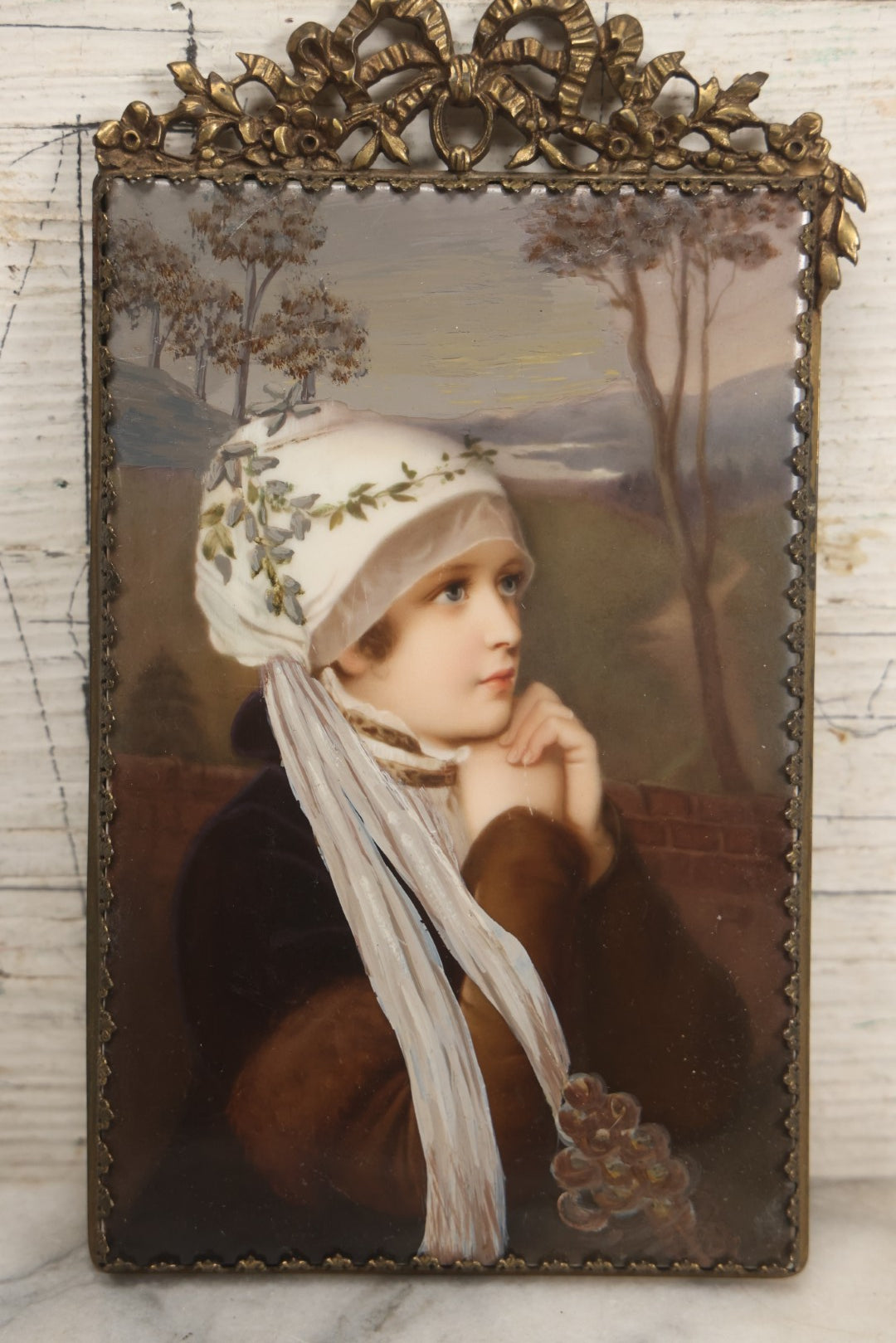 Lot 012 - Antique Painted Porcelain Tile Of Young Praying Woman In Brass Frame With Crest, Note Large Diagonal Crack Through Tile And Multiple Cracks From Upper Left Corner Damage, 4-7/8" x 9-1/8"