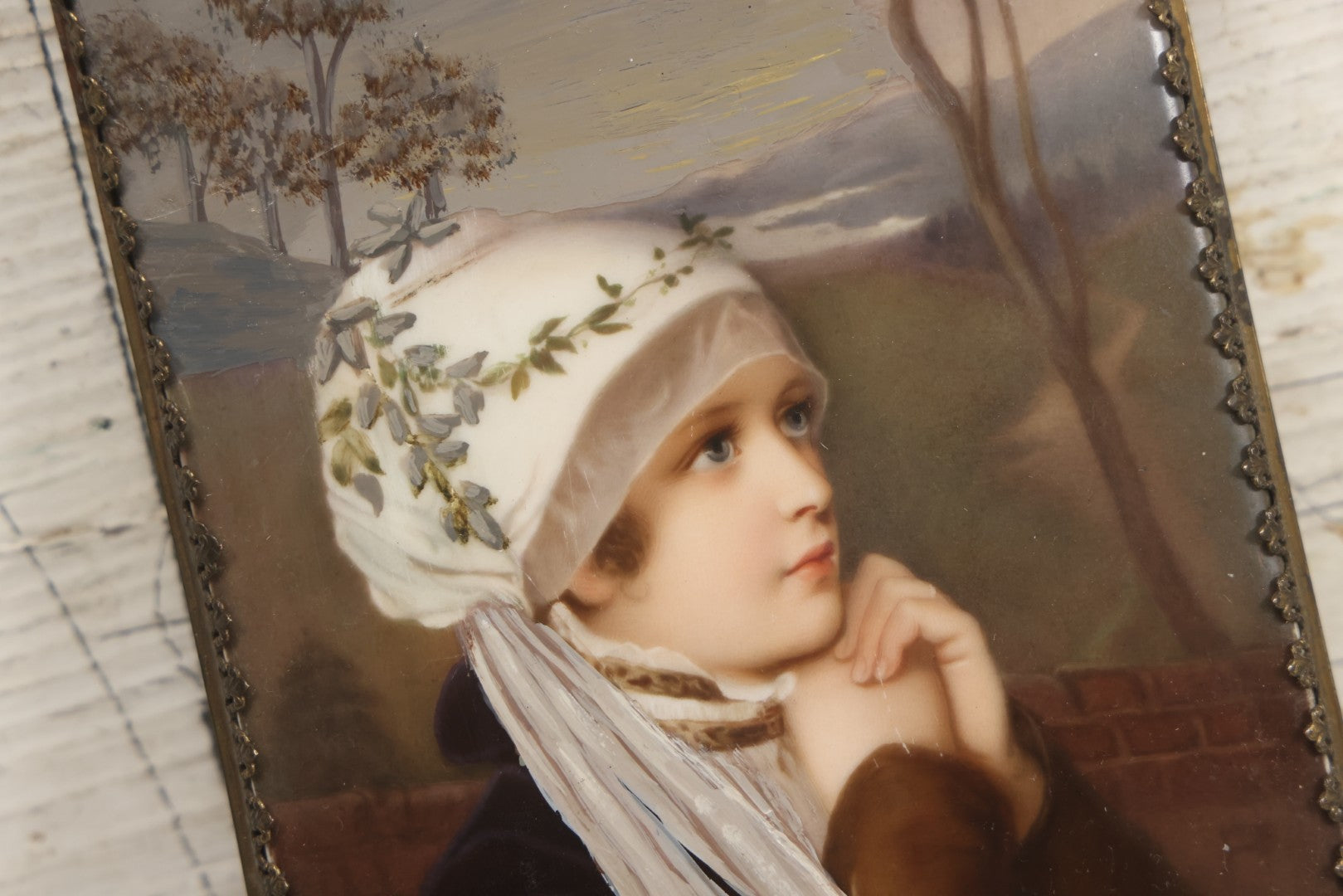 Lot 012 - Antique Painted Porcelain Tile Of Young Praying Woman In Brass Frame With Crest, Note Large Diagonal Crack Through Tile And Multiple Cracks From Upper Left Corner Damage, 4-7/8" x 9-1/8"