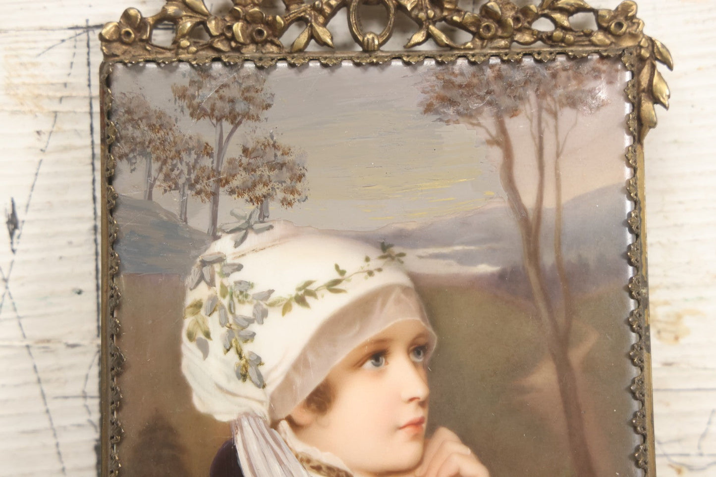 Lot 012 - Antique Painted Porcelain Tile Of Young Praying Woman In Brass Frame With Crest, Note Large Diagonal Crack Through Tile And Multiple Cracks From Upper Left Corner Damage, 4-7/8" x 9-1/8"