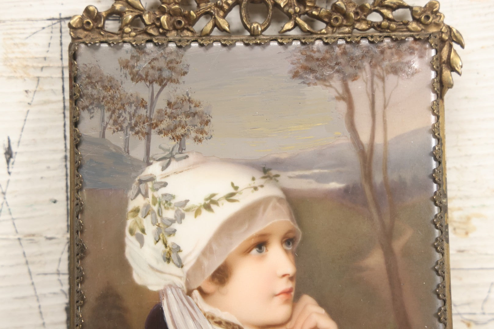 Lot 012 - Antique Painted Porcelain Tile Of Young Praying Woman In Brass Frame With Crest, Note Large Diagonal Crack Through Tile And Multiple Cracks From Upper Left Corner Damage, 4-7/8" x 9-1/8"