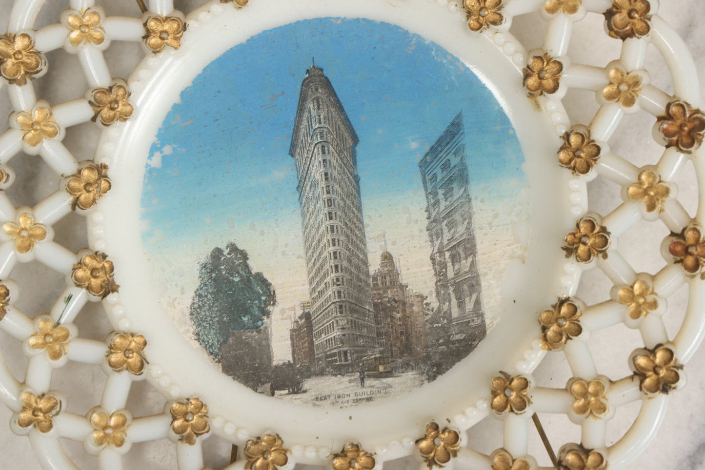 Lot 047 - Antique Milkglass Plate With Lattice Edge And Hand-Colored Transferware Image Of The Flatiron Building, New York City, With Forget-Me-Not Pattern And Brass Plate Hanger