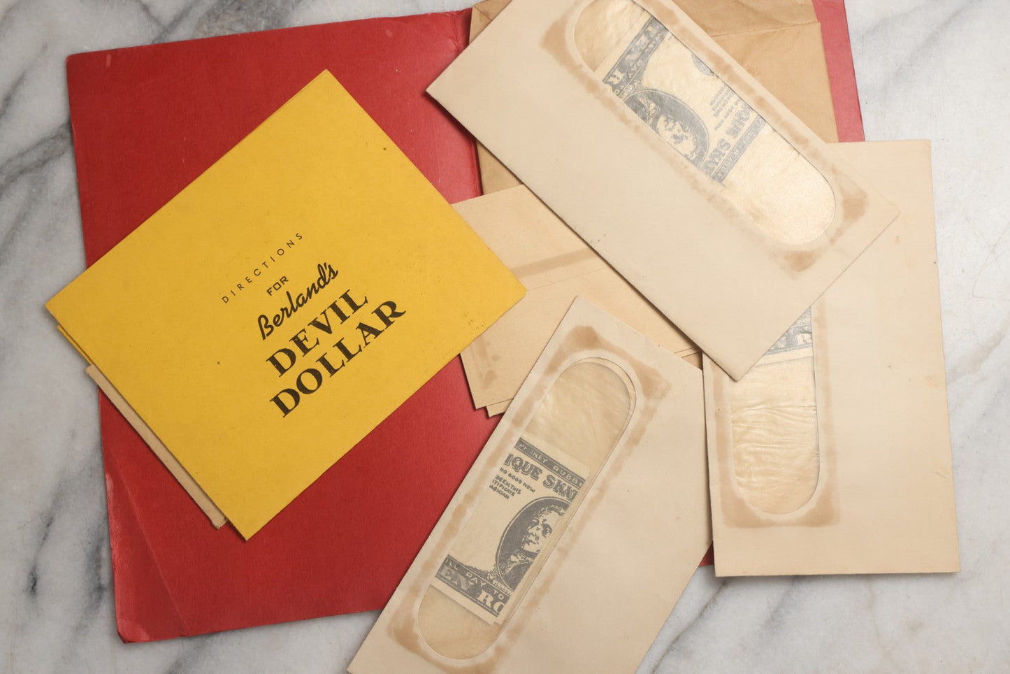 Lot 092 - Pair Of Vintage Berland's Magic Trick Folders Including Tear-A-Bill And Devil Dollar With Instructions, Props, And Envelopes, Completeness Not Verified
