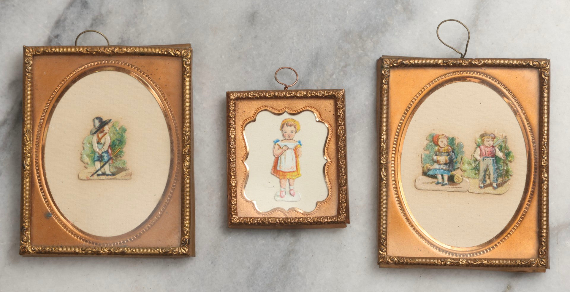 Lot 098 - Trio Of Antique Miniature Die-Cut Chromolithograph Scrap Figures In 1/9th And 1/16th Plate Photo Frames, Including Girl With Muff & Boy With Scythe, Boy With Sword, And Girl In Yellow Dress, All With Backing And Wire Loops