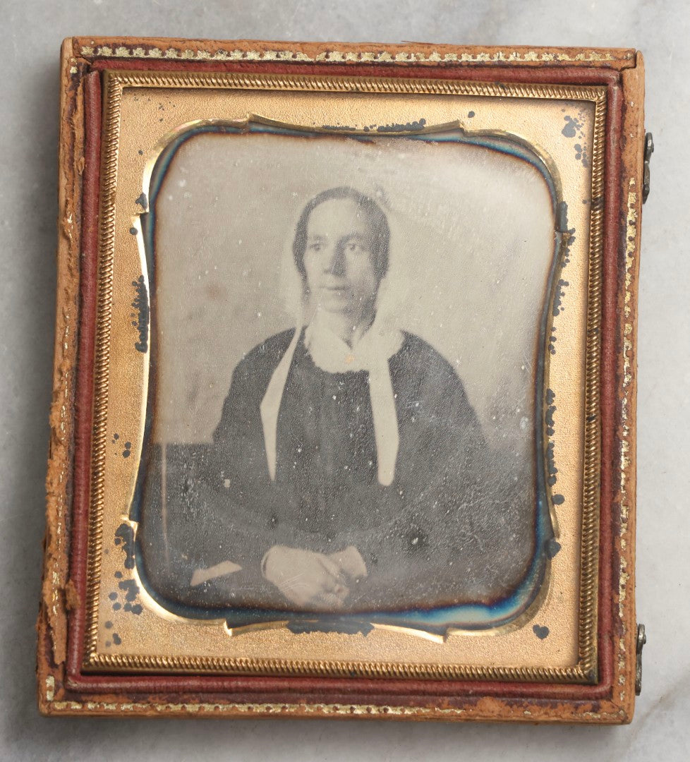 Lot 099 - Antique 1/6th Plate Daguerreotype Photograph Of Worried-Looking Middle-Aged Woman In White Bonnet With Long Ties, Hands Folded In Lap, In Half Leatherette Union Case