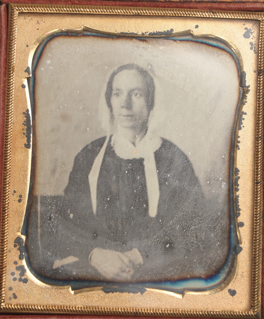 Lot 099 - Antique 1/6th Plate Daguerreotype Photograph Of Worried-Looking Middle-Aged Woman In White Bonnet With Long Ties, Hands Folded In Lap, In Half Leatherette Union Case