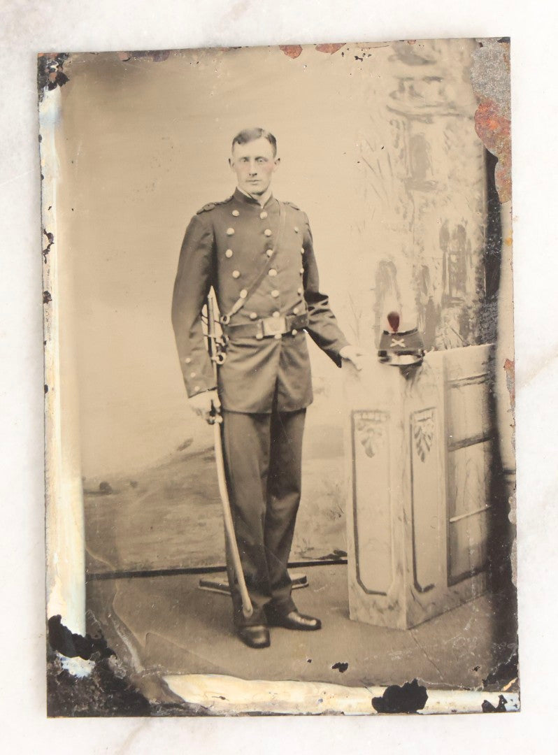 Lot 108 - Antique Tintype Photograph Of Uniformed Militiaman In Double-Breasted Coat With Shoulder Scales And Sword, Kepi On Pedestal, In Studio Setting