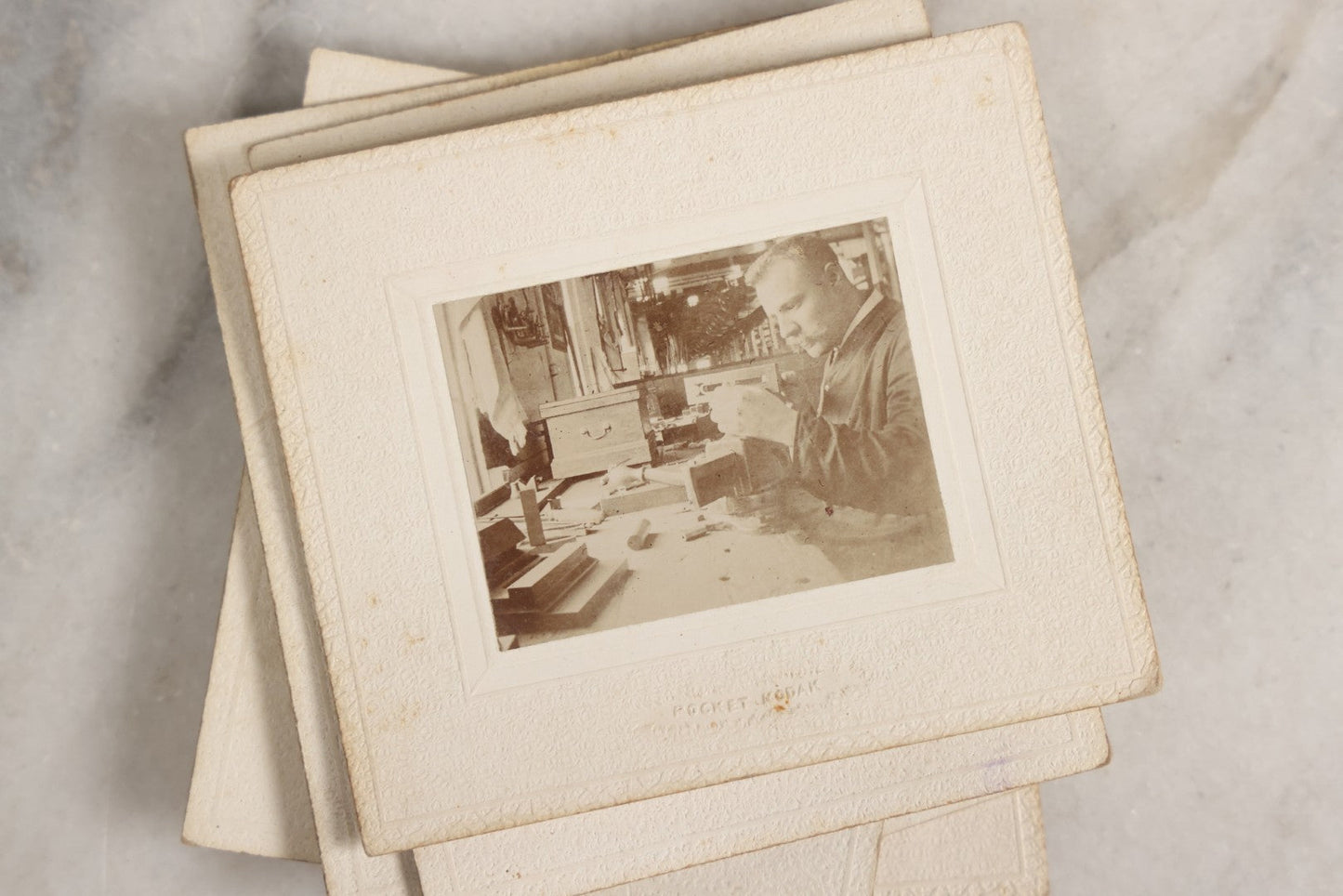 Lot 151 - Antique Box Lot Of Fifteen “Pocket Kodak” Miniature Boarded Photographs Including Dog On Stool, Boys Smoking Pipes, And Man In Workshop, With Camp Alger Flag Pin And American Views Co. Trade Card In John D. Cutter & Co. Chromolithograph Box