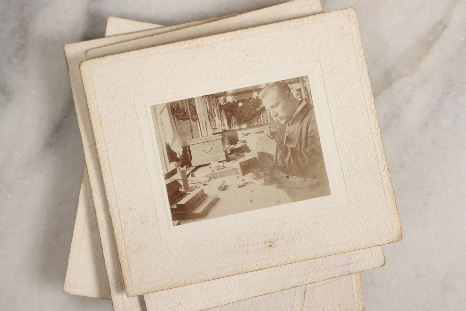 Lot 151 - Antique Box Lot Of Fifteen “Pocket Kodak” Miniature Boarded Photographs Including Dog On Stool, Boys Smoking Pipes, And Man In Workshop, With Camp Alger Flag Pin And American Views Co. Trade Card In John D. Cutter & Co. Chromolithograph Box