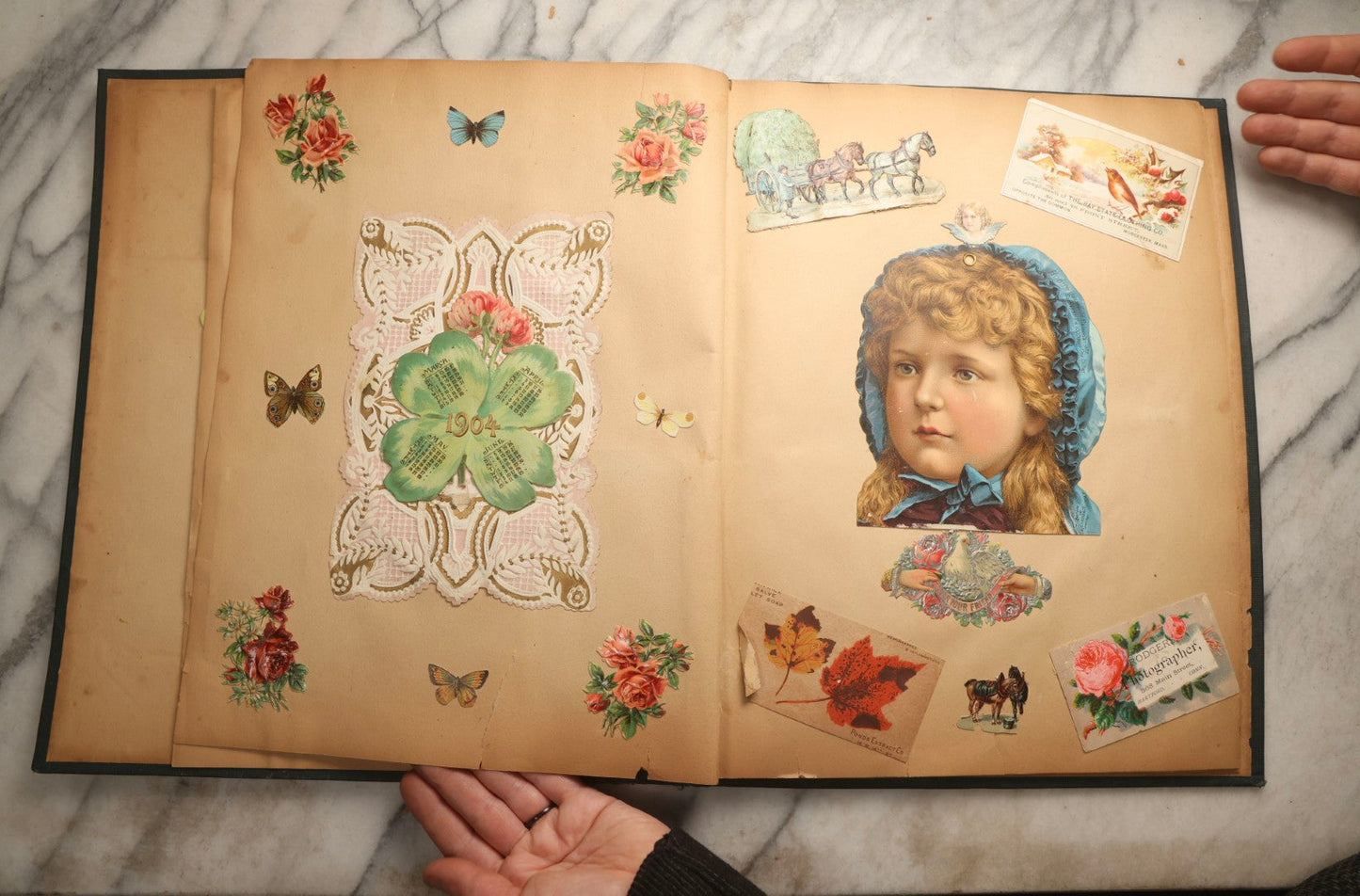 Lot 096 - Antique "The Nonpareil" Scrapbook, Puppies Illustration On Cover, With 100+ Trade Cards, Die Cuts, And Greeting Cards Featuring Children, Butterflies, And Flowers, Circa 1900-1906, Note Binding Detached