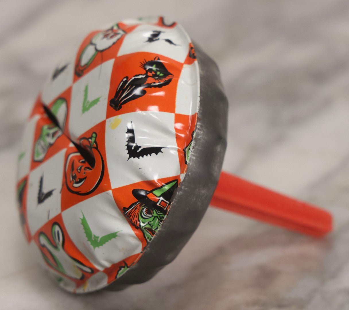 Lot 048 - Vintage Round Halloween Tin Lithograph Noisemaker With Orange And White Checkered Pattern Featuring Black Cat, Witch, Ghost, Bat, Skull, And Jack-O'-Lantern J.O.L. Characters