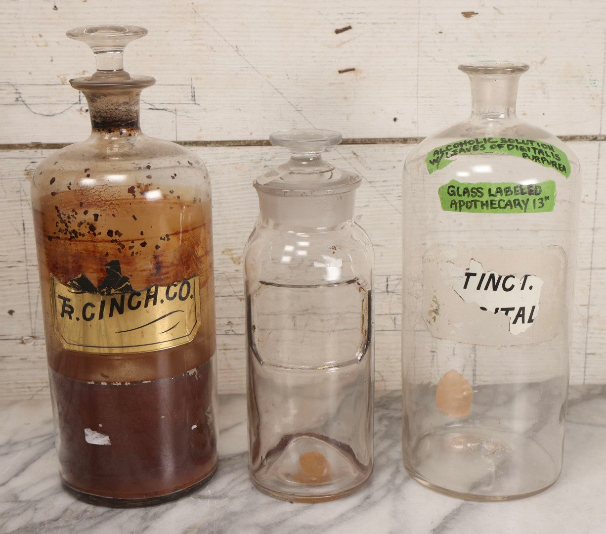 Lot 090 - Trio Of Antique Apothecary Glass Bottles With Ground Stoppers, Mixed Sizes, Worn And Partially Detached Labels, Residue And Staining, Poor As-Found Condition
