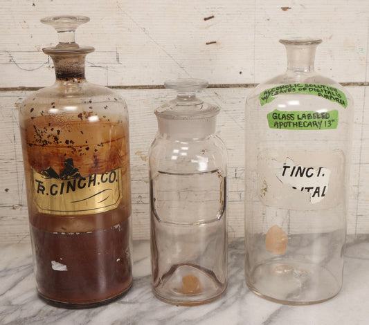 Lot 090 - Trio Of Antique Apothecary Glass Bottles With Ground Stoppers, Mixed Sizes, Worn And Partially Detached Labels, Residue And Staining, Poor As-Found Condition
