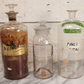 Lot 090 - Trio Of Antique Apothecary Glass Bottles With Ground Stoppers, Mixed Sizes, Worn And Partially Detached Labels, Residue And Staining, Poor As-Found Condition