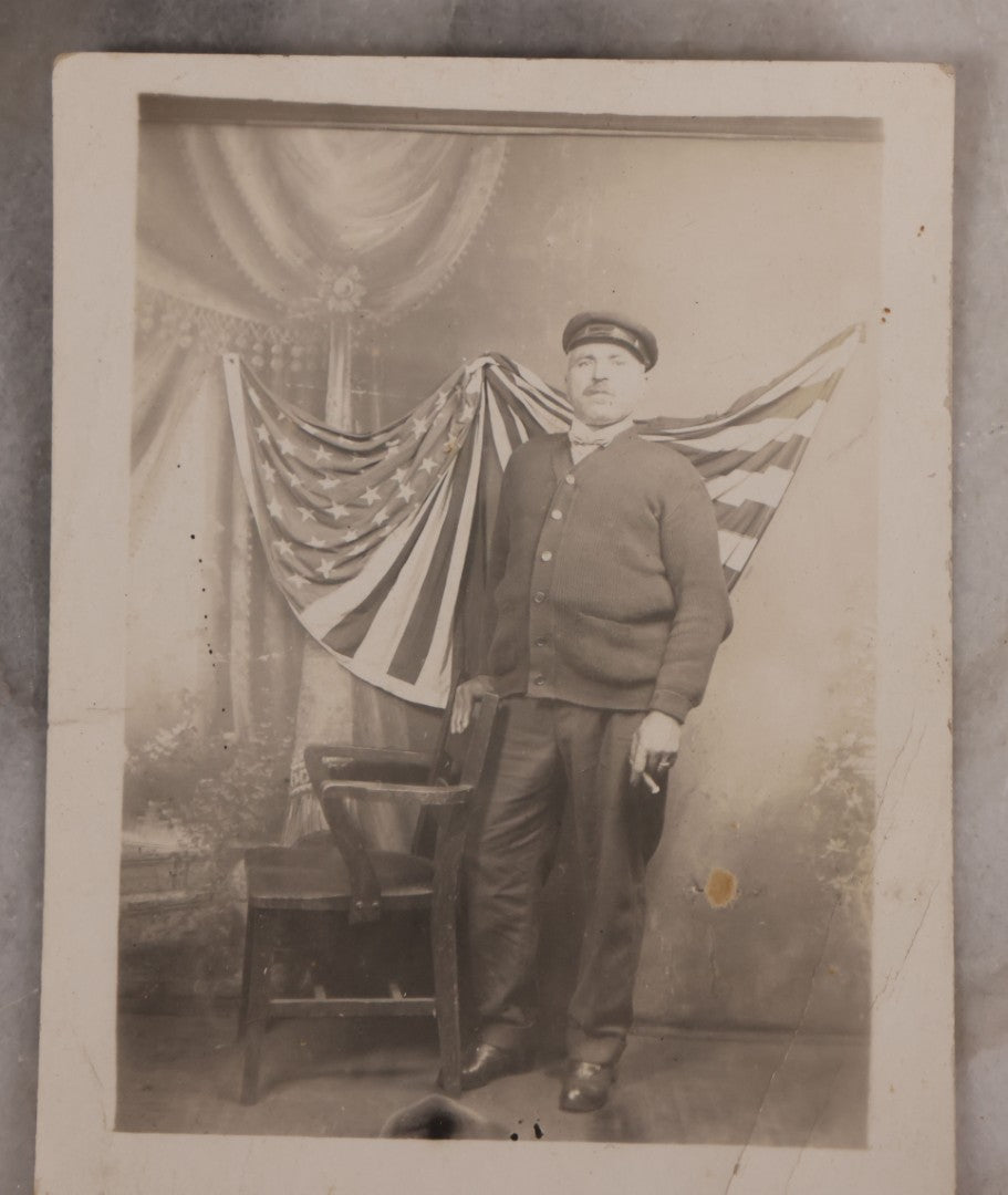 Lot 174 - Antique Real Photo Postcard R.P.P.C. Of Man In Uniform And Cap With Cigarette Before American Flag Backdrop, Circa 1910s