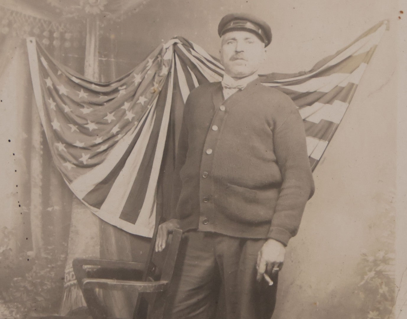 Lot 174 - Antique Real Photo Postcard R.P.P.C. Of Man In Uniform And Cap With Cigarette Before American Flag Backdrop, Circa 1910s