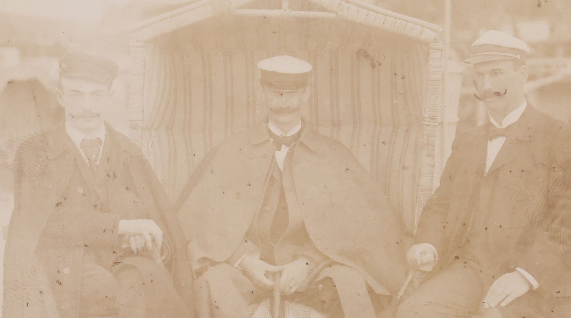 Lot 179 - Antique Board-Mounted Photograph Of Three Mustachioed Men Posed On Beach In Suits With Capes And Walking Sticks Before Striped Beach Windbreak, Westerland, Sylt, Photographed By A. Gabel
