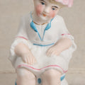 Lot 180 - Antique Bisque Figure of a Child With Pink Hat Seated on a Chamber Pot, Likely German, Note Severe Crack Across Midsection, 4-1/4" Height