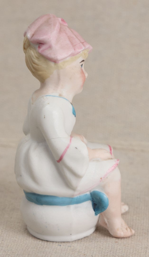Lot 180 - Antique Bisque Figure of a Child With Pink Hat Seated on a Chamber Pot, Likely German, Note Severe Crack Across Midsection