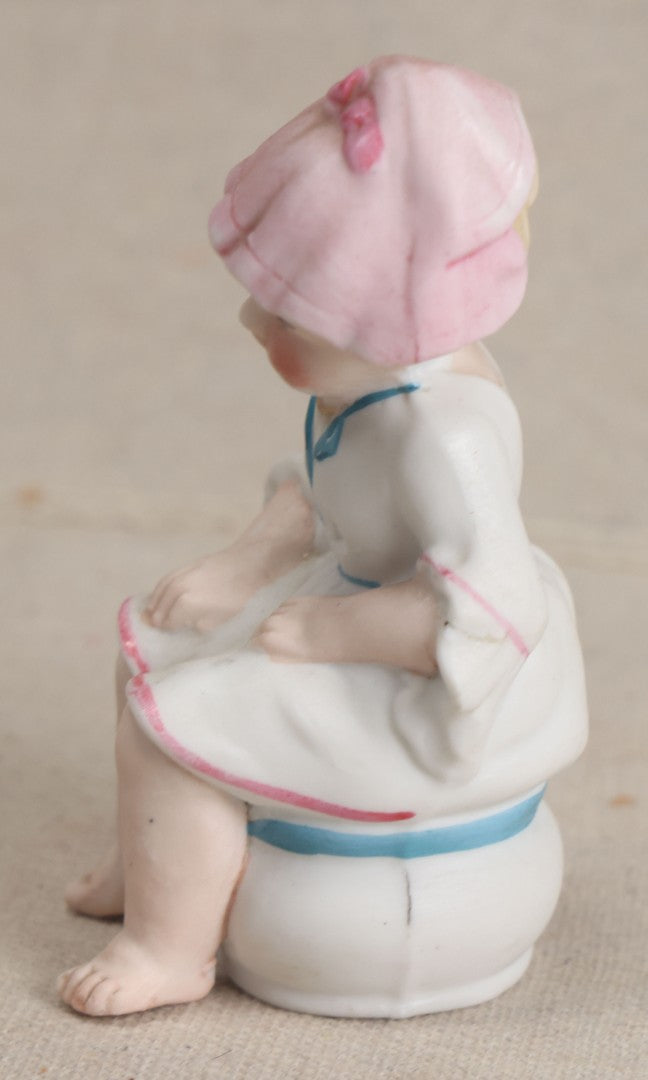 Lot 180 - Antique Bisque Figure of a Child With Pink Hat Seated on a Chamber Pot, Likely German, Note Severe Crack Across Midsection