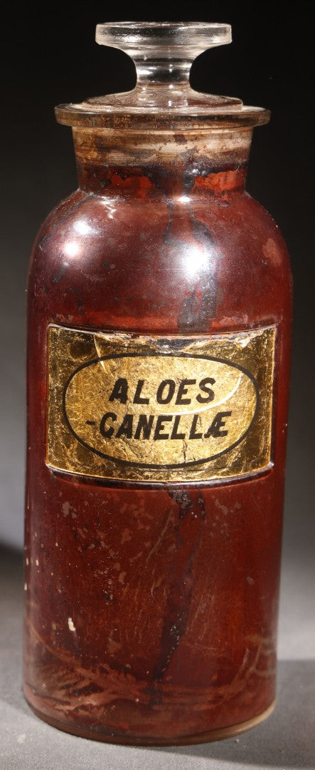 Lot 015 - Antique Apothecary Glass Jar, "Aloes Canellae" (Aloe And Canella Bark), Reverse-Painted Gold Glass Label With Oval Cartouche, Glass Stopper, Manufactured By Whitall Tatum Company, U.S.A..