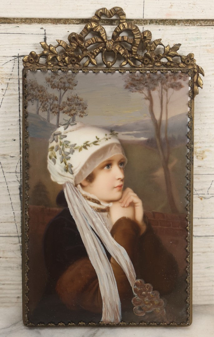 Lot 012 - Antique Painted Porcelain Tile Of Young Woman in White Head Scarf Posed Before Landscape with Clasped Hands, In Brass Frame With Crest, Note Large Crack, 4-7/8" x 9-1/8"