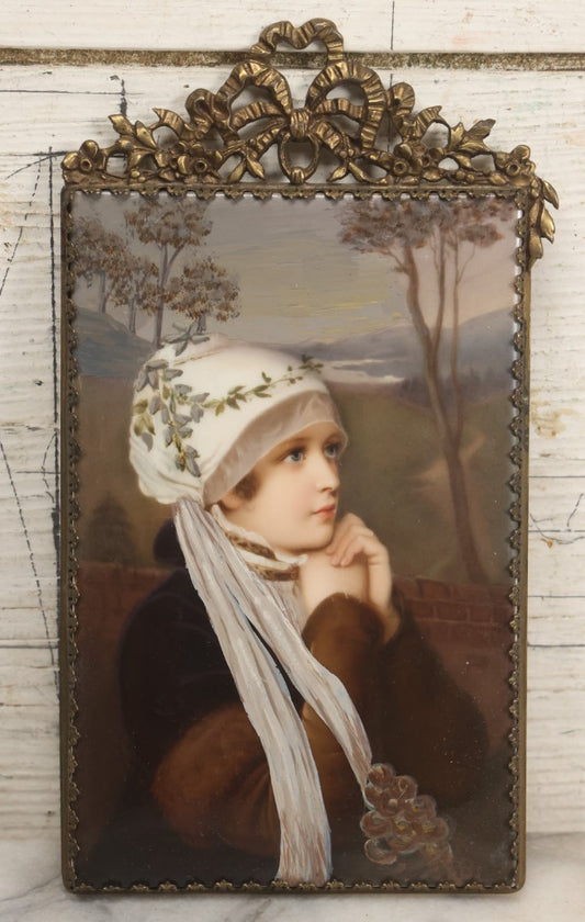 Lot 012 - Antique Painted Porcelain Tile Of Young Woman in White Head Scarf Posed Before Landscape with Clasped Hands, In Brass Frame With Crest, Note Large Crack, 4-7/8" x 9-1/8"