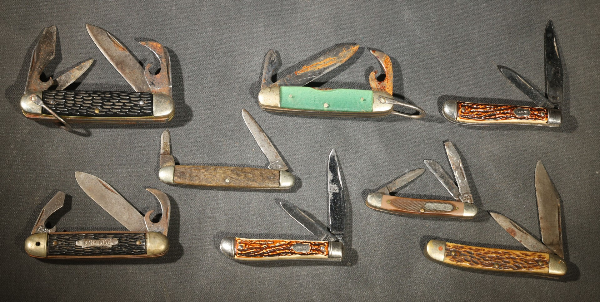 Grouping of Seven Vintage Folding Pocket Knives Including Multi-Tool Camp Knives, Stockman, and Trapper Styles with Bone, Jigged, and Composite Handles